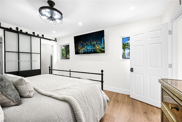 bedroom with light wood finished floors, a barn door, baseboards, and recessed lighting
