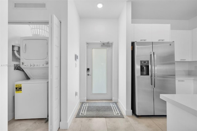 laundry room featuring stacked washer / dryer, light tile patterned floors, laundry area, visible vents, and baseboards