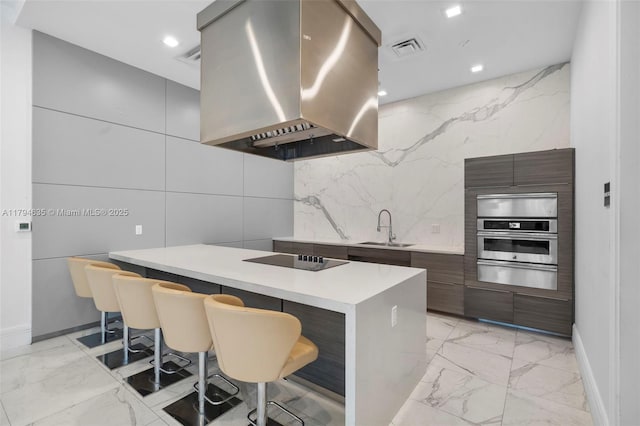 kitchen with island exhaust hood, modern cabinets, stainless steel oven, and a sink