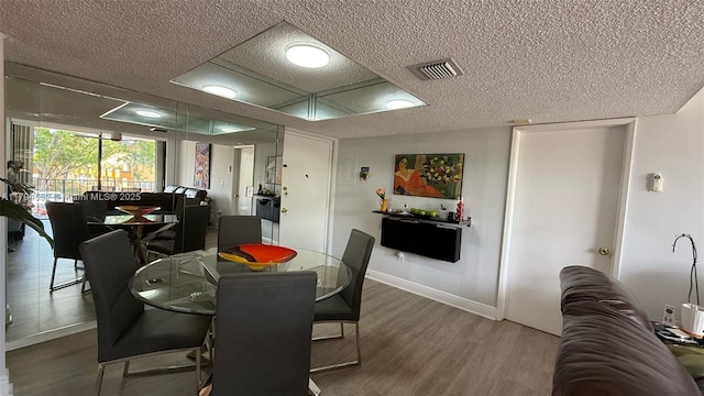 dining room with a textured ceiling, visible vents, wood finished floors, and baseboards