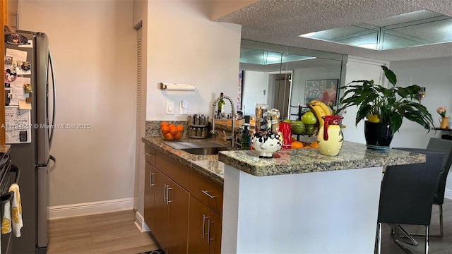 bar featuring wood finished floors, a sink, freestanding refrigerator, baseboards, and wet bar