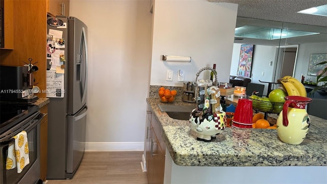 kitchen with brown cabinetry, stainless steel fridge with ice dispenser, baseboards, light stone countertops, and range with electric stovetop