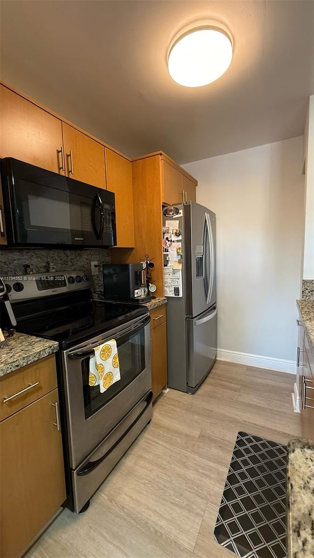 kitchen featuring stone countertops, brown cabinetry, appliances with stainless steel finishes, baseboards, and light wood-style floors