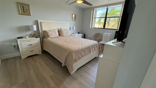 bedroom featuring baseboards, ceiling fan, a textured ceiling, and wood finished floors