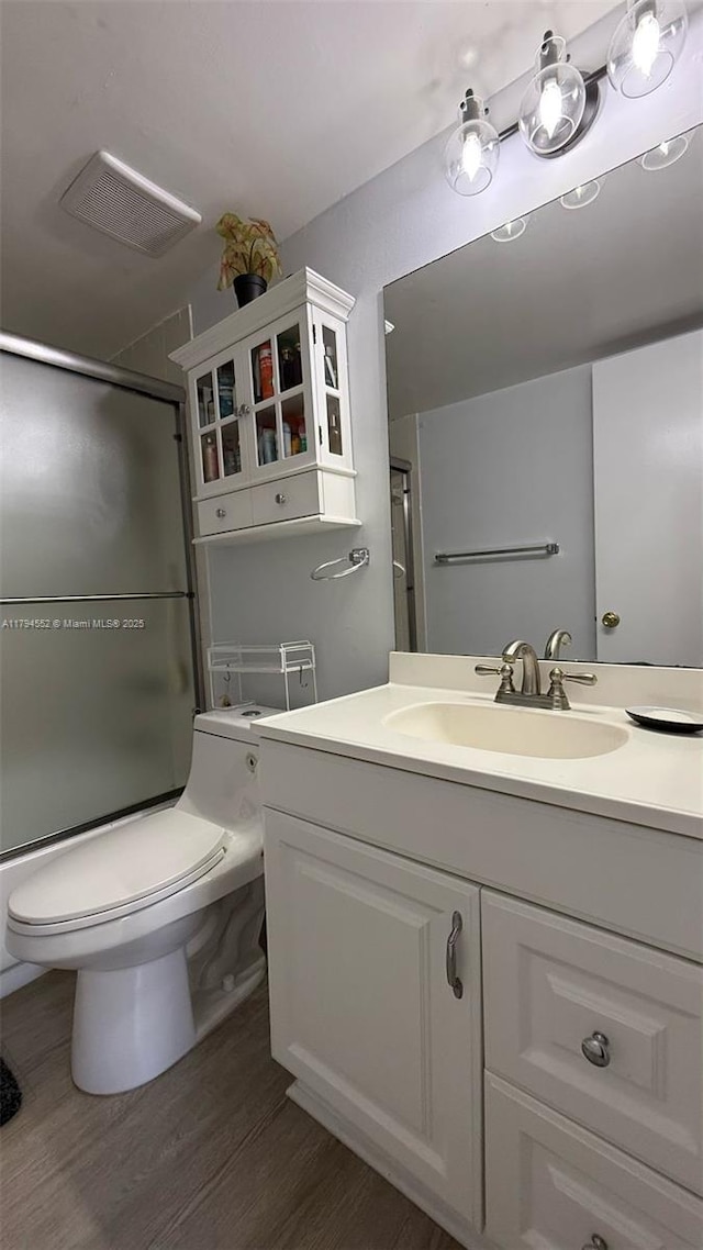 bathroom featuring toilet, visible vents, shower / bath combination with glass door, vanity, and wood finished floors