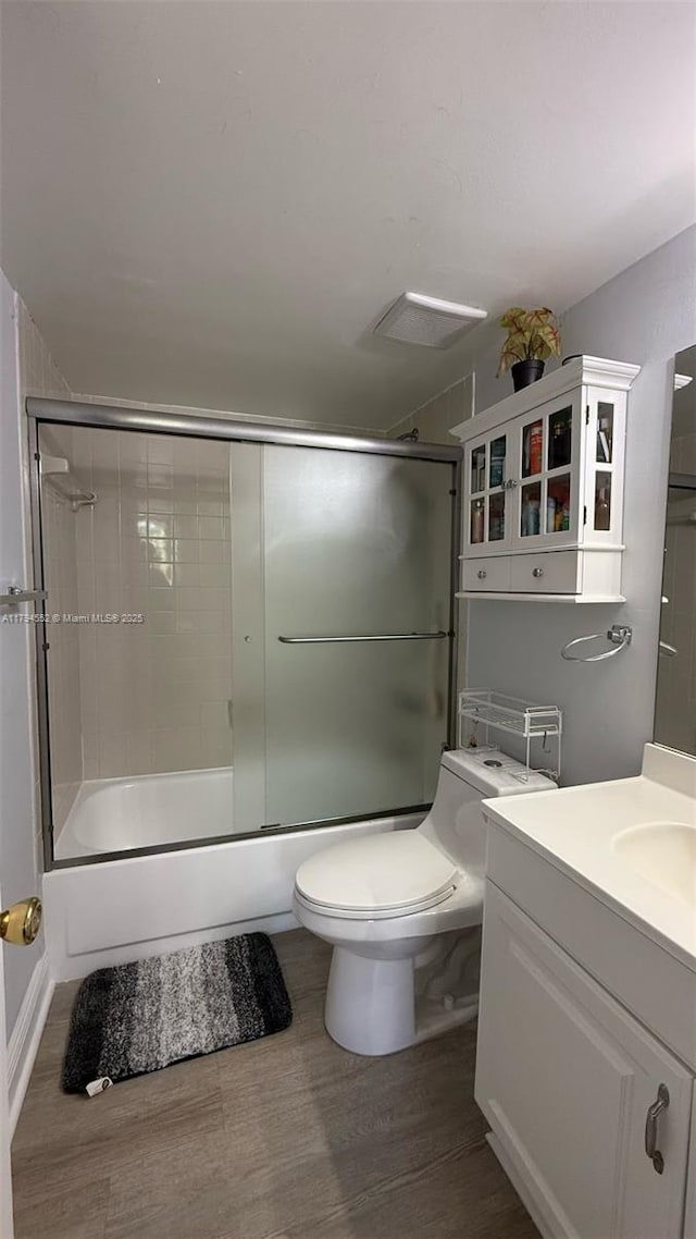 full bathroom featuring toilet, enclosed tub / shower combo, wood finished floors, and vanity