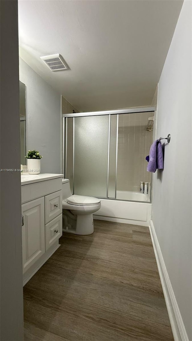 bathroom featuring toilet, enclosed tub / shower combo, visible vents, vanity, and wood finished floors
