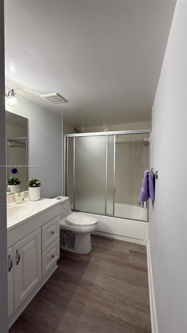 bathroom with toilet, wood finished floors, vanity, visible vents, and combined bath / shower with glass door