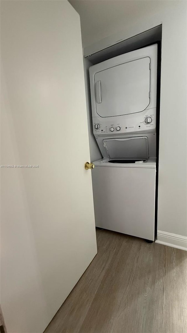 washroom featuring laundry area, stacked washer and clothes dryer, baseboards, and wood finished floors