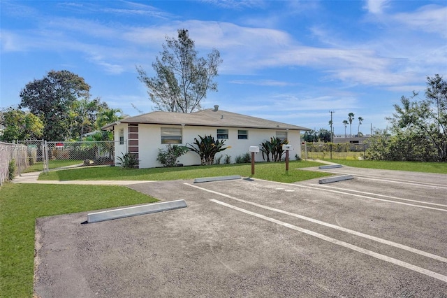 view of front facade featuring stucco siding, a front lawn, fence, and uncovered parking