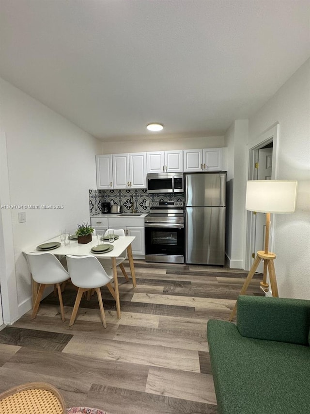 kitchen featuring stainless steel appliances, white cabinetry, baseboards, light wood-style floors, and decorative backsplash