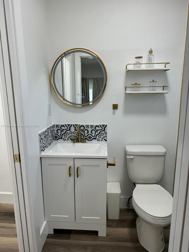 half bath with toilet, baseboards, vanity, and wood finished floors