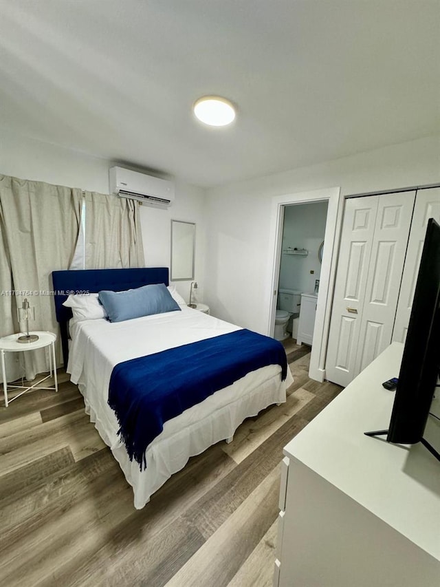 bedroom with a wall mounted air conditioner, ensuite bathroom, a closet, and wood finished floors