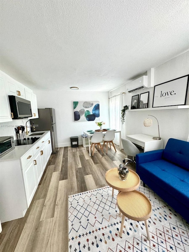 living room with light wood-type flooring, a wall unit AC, and a textured ceiling