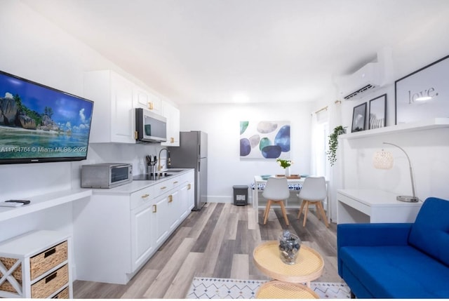 interior space featuring appliances with stainless steel finishes, a wall unit AC, light countertops, white cabinets, and light wood-type flooring