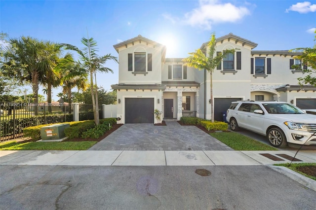 mediterranean / spanish house featuring stucco siding, a garage, fence, and decorative driveway