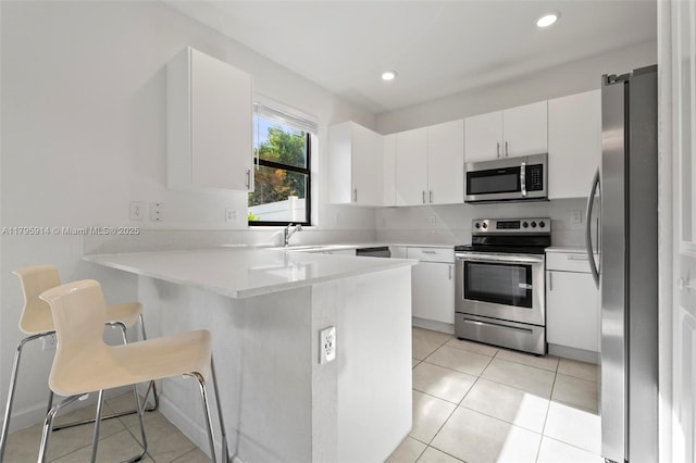 kitchen with a peninsula, a breakfast bar area, light countertops, white cabinets, and appliances with stainless steel finishes