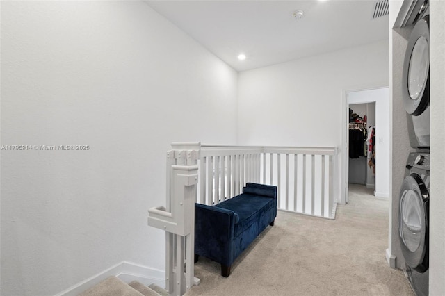 living area with an upstairs landing, visible vents, light carpet, stacked washing maching and dryer, and baseboards