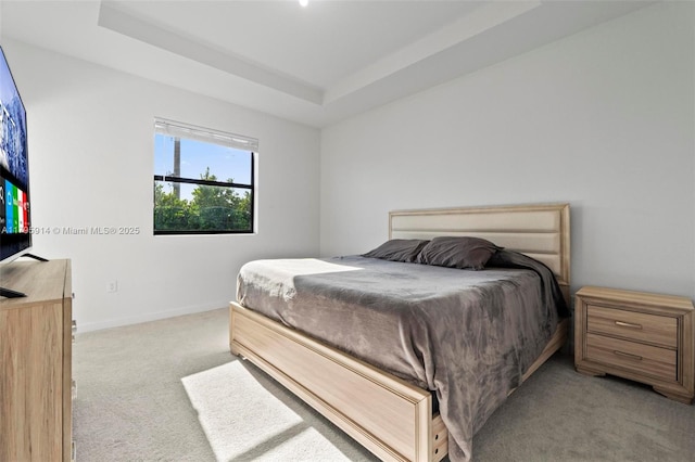 bedroom featuring light colored carpet, baseboards, and a tray ceiling