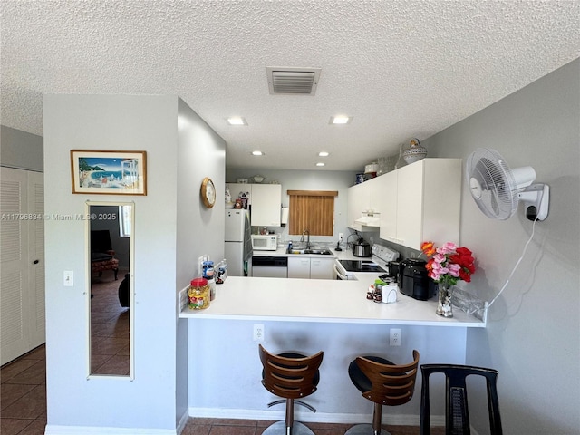 kitchen featuring a sink, white appliances, a breakfast bar, visible vents, and tile patterned floors