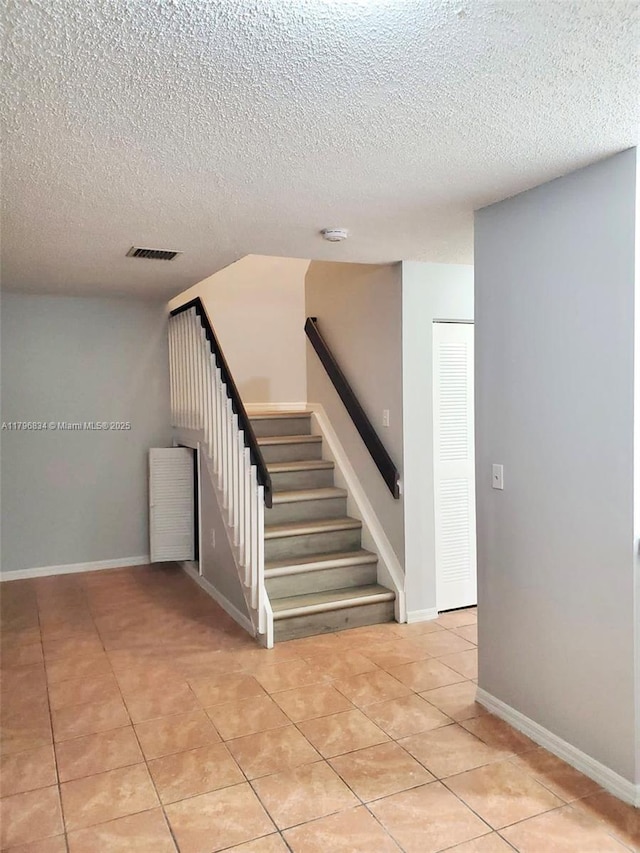 stairs with a textured ceiling, baseboards, visible vents, and tile patterned floors