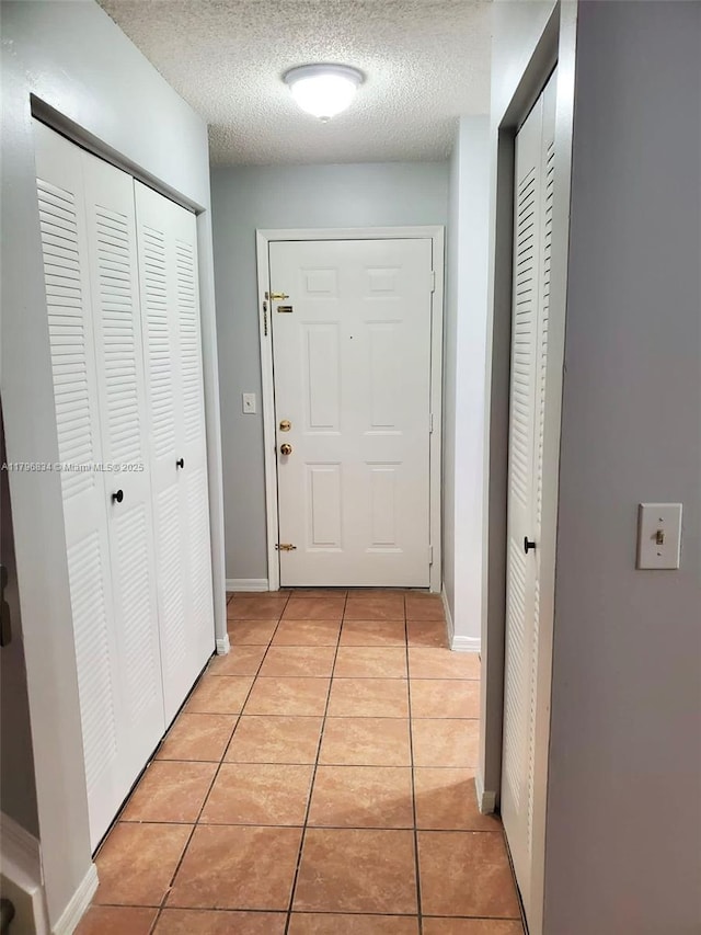 hallway with baseboards, light tile patterned flooring, and a textured ceiling