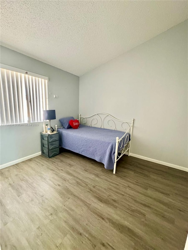 bedroom featuring a textured ceiling, baseboards, and wood finished floors