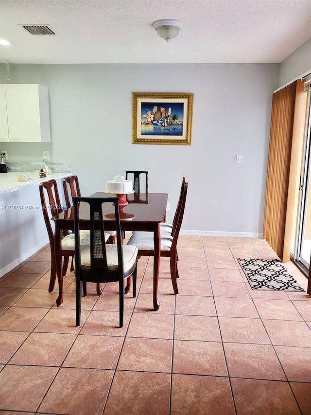 dining room with light tile patterned flooring, a textured ceiling, baseboards, and visible vents