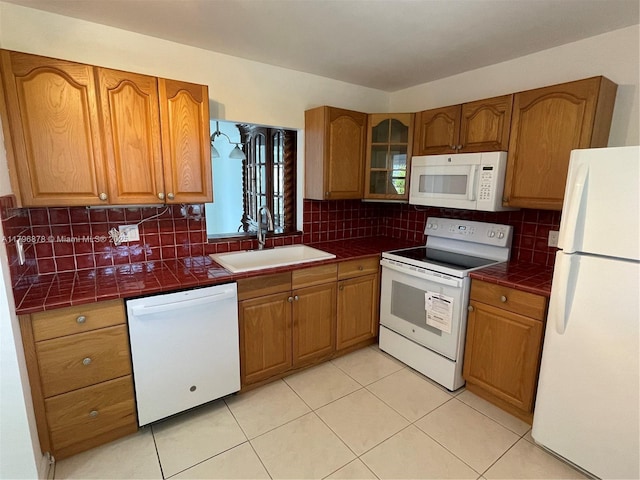 kitchen featuring brown cabinetry, tile counters, a sink, and white appliances