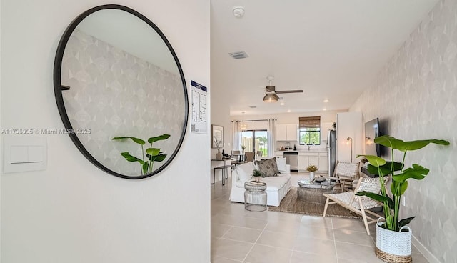 living room featuring visible vents, a ceiling fan, light tile patterned floors, baseboards, and wallpapered walls