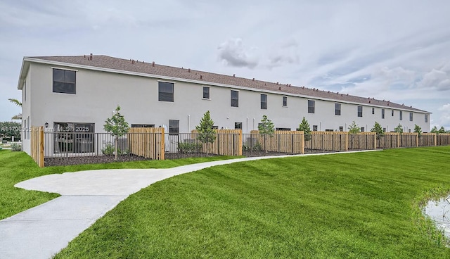 rear view of house with a yard, stucco siding, and fence