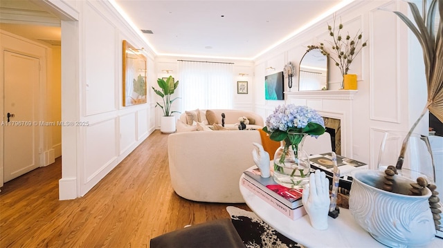 living area featuring light wood-style floors, a fireplace, a decorative wall, and visible vents