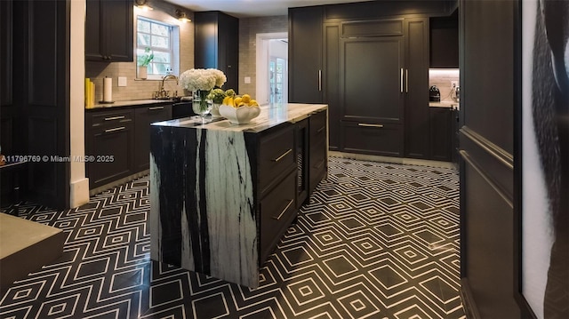 kitchen featuring tile patterned floors, tasteful backsplash, dark cabinetry, and a sink
