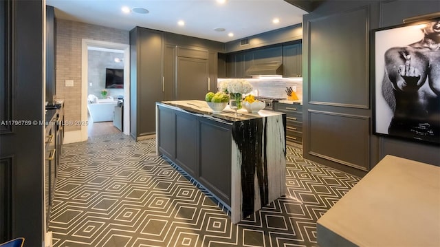 kitchen with recessed lighting, under cabinet range hood, backsplash, dark cabinets, and a kitchen island