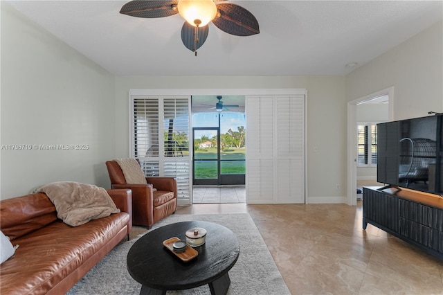 living area featuring baseboards, light tile patterned floors, and ceiling fan
