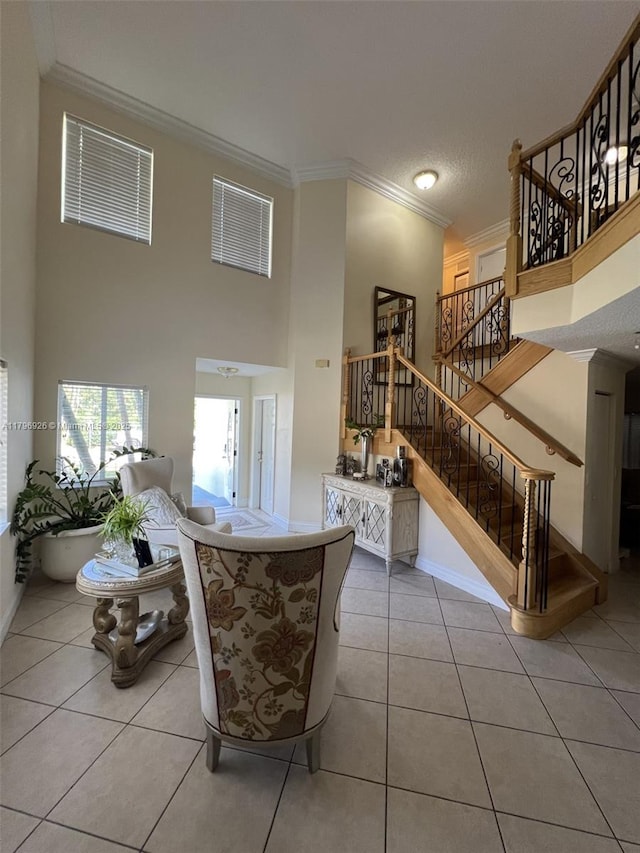 living area featuring baseboards, stairs, tile patterned flooring, crown molding, and a high ceiling