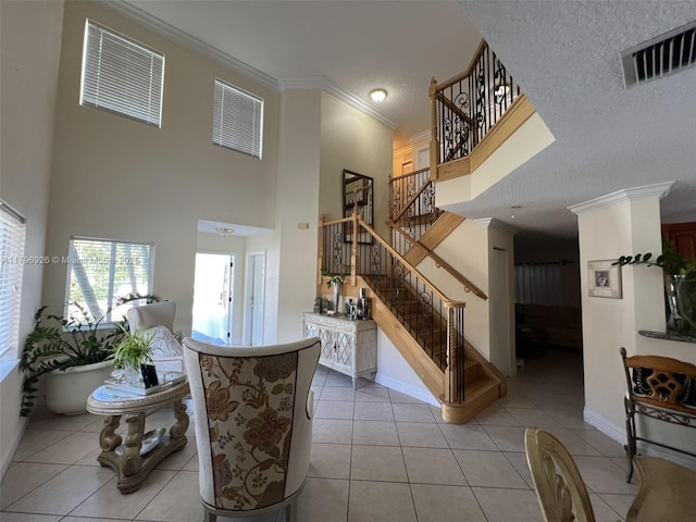 interior space featuring visible vents, stairway, crown molding, light tile patterned floors, and a high ceiling