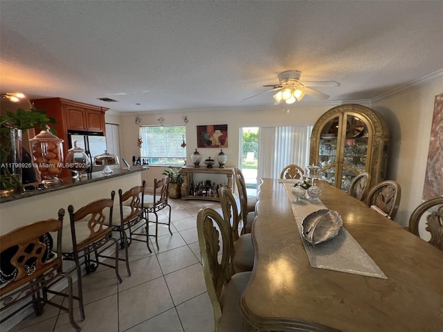 dining space featuring ornamental molding, light tile patterned flooring, a textured ceiling, and a ceiling fan