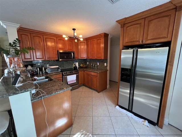 kitchen featuring a peninsula, brown cabinets, backsplash, a notable chandelier, and appliances with stainless steel finishes