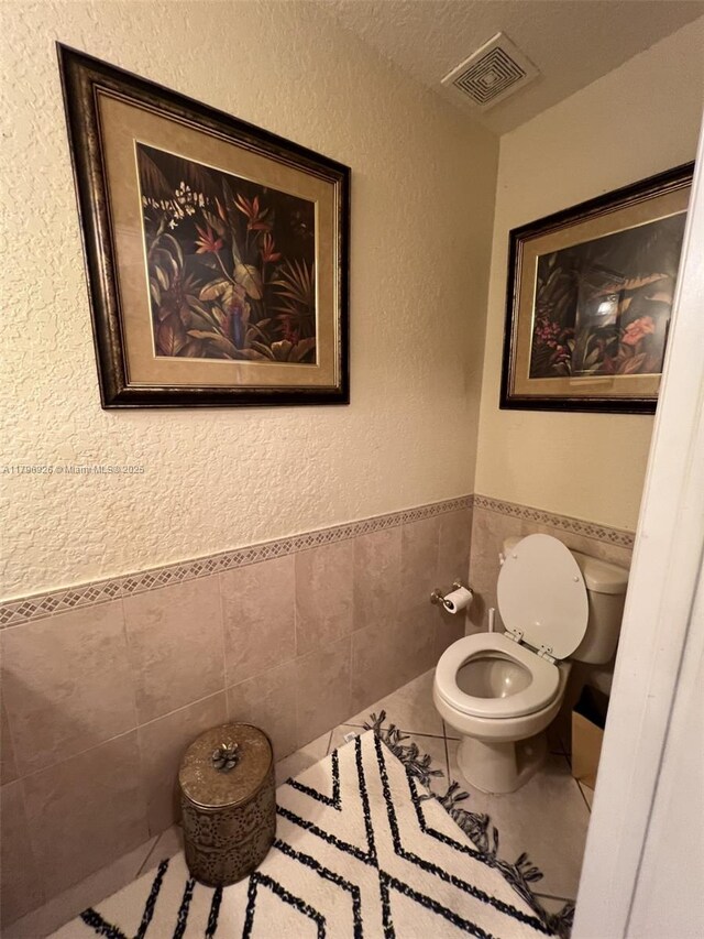 bathroom featuring tile walls, toilet, visible vents, and a textured wall