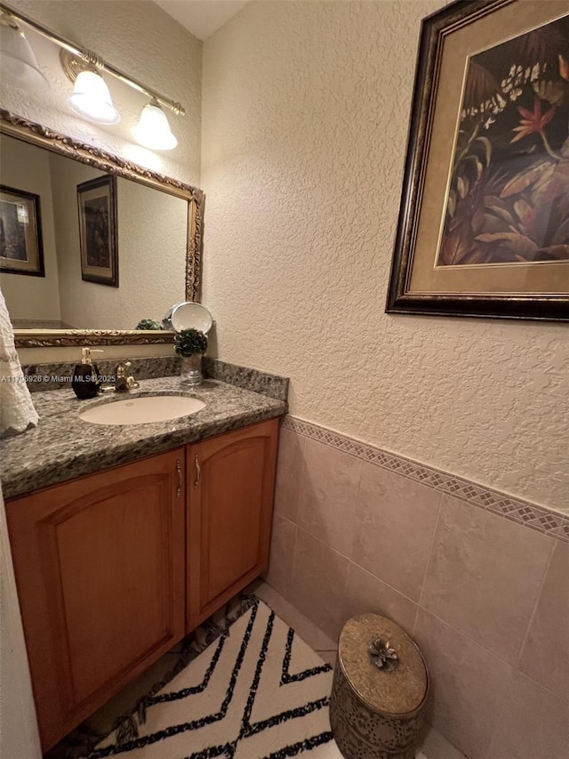 bathroom with vanity, tile walls, a textured wall, and a wainscoted wall