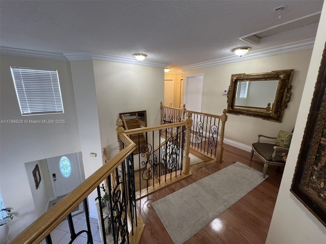 hall with wood finished floors, an upstairs landing, attic access, visible vents, and ornamental molding