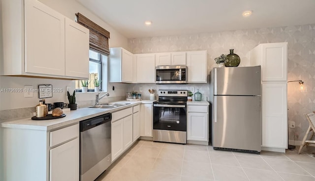 kitchen with a sink, wallpapered walls, white cabinetry, light countertops, and appliances with stainless steel finishes