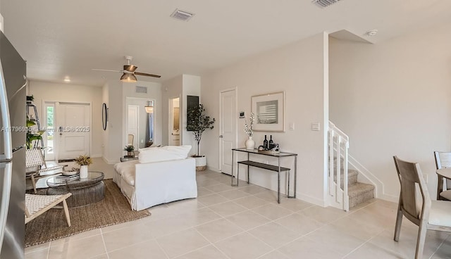 living area featuring light tile patterned floors, a ceiling fan, visible vents, baseboards, and stairway