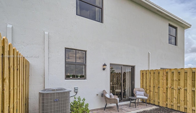 back of property featuring central air condition unit, stucco siding, and fence