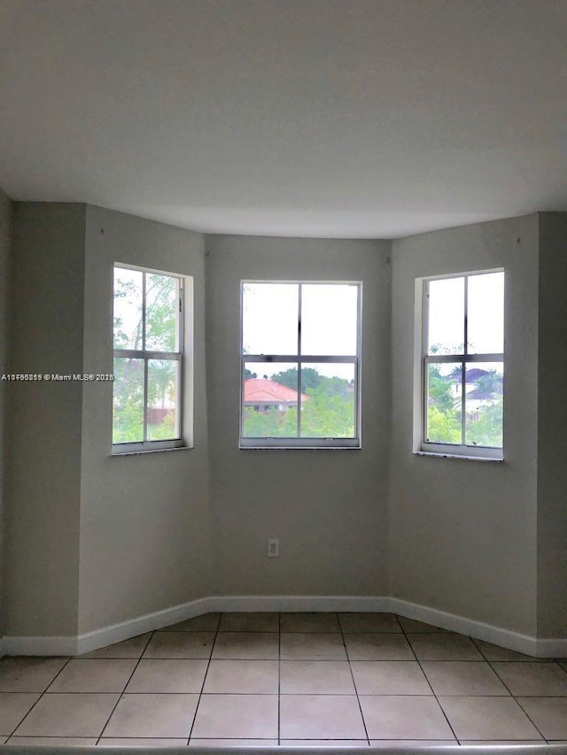 spare room with light tile patterned flooring, baseboards, and plenty of natural light