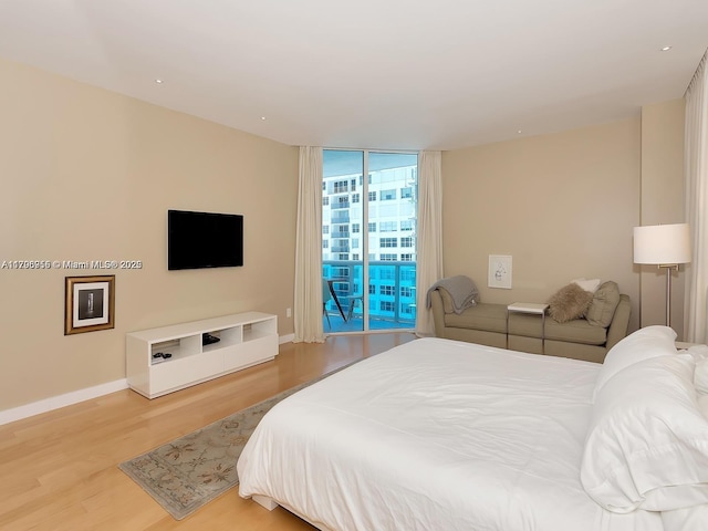 bedroom with floor to ceiling windows, wood finished floors, baseboards, and access to exterior