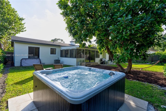 exterior space with a sunroom, a hot tub, fence, and a lawn