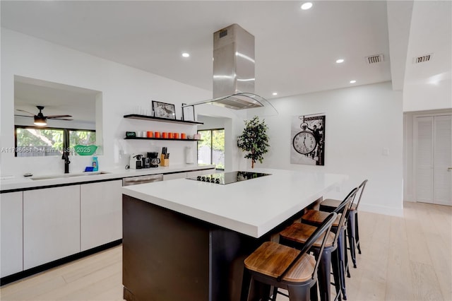 kitchen featuring a sink, black electric cooktop, island range hood, and visible vents