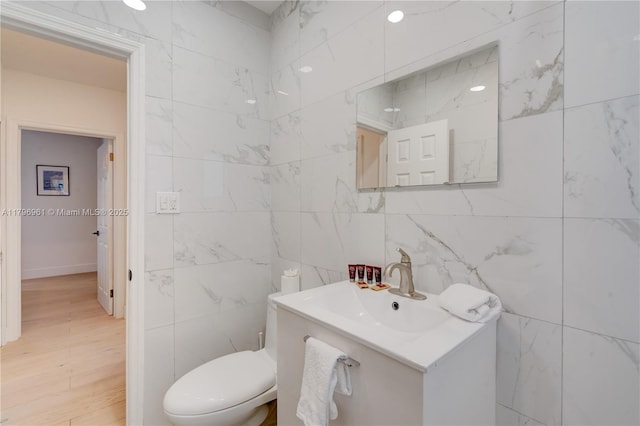 bathroom featuring tile walls, toilet, wood finished floors, and vanity
